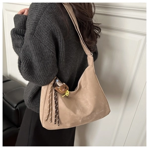 Detail of beige shoulder bag with plush bear charm and colorful woven cord decoration
