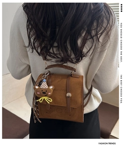Brown faux suede mini backpack with plush bear charm worn over a white sweater