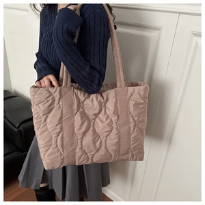 Champagne gold quilted puffer tote bag in lightweight nylon worn by a model in interior setting