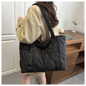 Detail view of black quilted puffer tote bag worn over the shoulder in a lifestyle setting