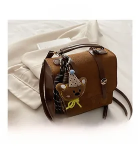 Detailed view of a brown vintage satchel with suede stitching and a cute teddy bear charm