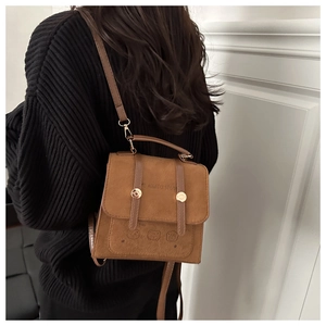 Detail of brown suede small square bag featuring metal buckles and cute bear embossing