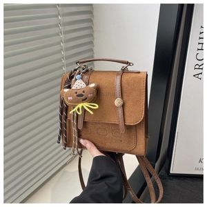 Detail of a brown faux suede handbag featuring a cute plush bear charm and handle