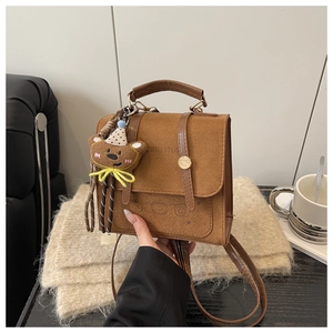 Detailed view of a brown suede handbag featuring a cute bear embossing and knit doll charm