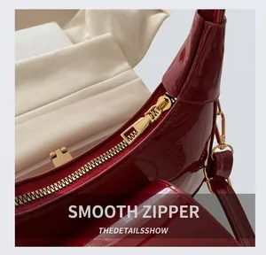 Detailed macro of smooth gold zipper on deep red patent leather shoulder bag