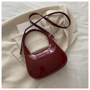 Close-up of glossy burgundy patent leather saddle bag with gold hardware and fine stitching