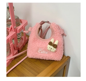 Detailed shot of pink fuzzy mini bag with rabbit charm and Cutie embroidery on a wooden table
