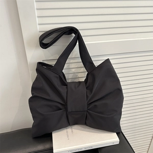 Minimalist black nylon bow-shaped shoulder bag on books with a clean aesthetic