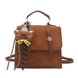 Brown suede mini handbag with cartoon bear print and cute plush charm on white background