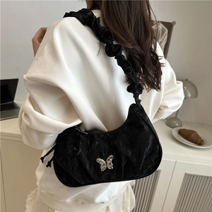 Chic black pleated underarm bag with silver butterfly buckle in a lifestyle setting