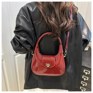 Detail of burgundy glossy patent leather crescent bag with adjustable strap and gold buckle