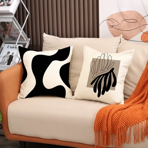 Modern black and white geometric pattern pillow covers on a cozy sofa with an orange throw