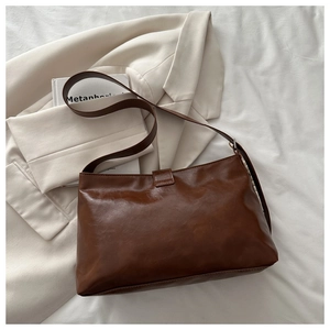 Detailed view of brown PU leather shoulder bag with oil wax texture on white blazer