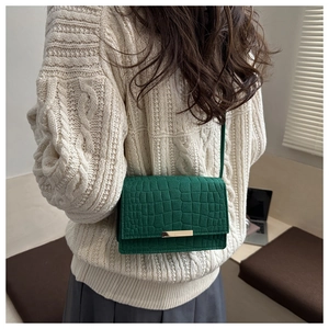 Détail du sac à main vert foncé motif crocodile avec fermoir doré sur le modèle