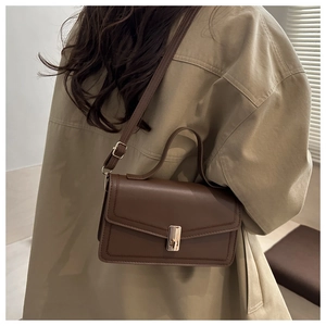 Detail of a dark brown vintage crossbody bag featuring a golden clasp on beige trench coat