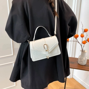 Sac à main blanc texturé avec boucle dorée porté par un mannequin en robe noire élégante