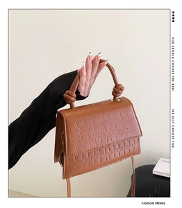 Detailed macro of brown crocodile pattern handbag with twisted handle and metal buckle