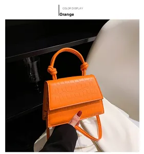 Detail view of orange faux leather handbag with crocodile pattern and knotted handle