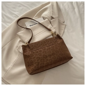 Détail du sac bandoulière imprimé léopard avec chaîne dorée sur un blazer blanc