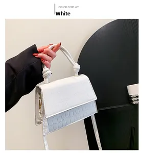Close-up of white crocodile texture handbag with knotted handle and golden hardware