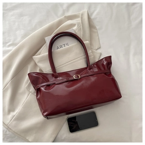 Close-up of luxury glossy wine red leather tote bag with elegant gold buckle detail