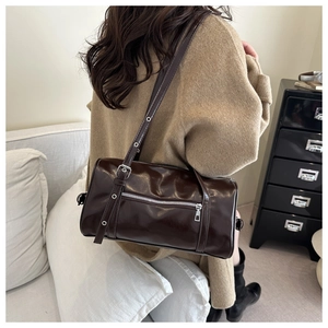 Detailed view of glossy dark brown Boston bag with adjustable metallic buckle straps
