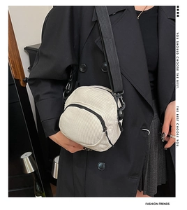 Close-up of a white corduroy crossbody bag with black straps worn by a model in a coat