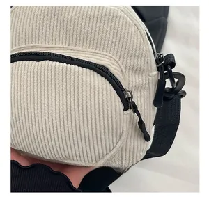 Detail showing white corduroy fabric texture and dual black zippers of the crossbody bag