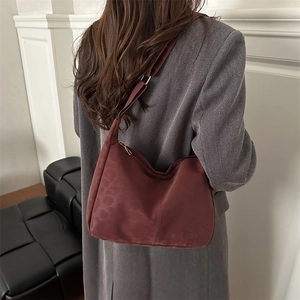 Burgundy leopard print crossbody bag worn with a grey blazer against a white wall