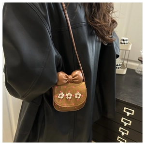 Détail d'un mini sac bandoulière marron avec nœud en cuir et fleurs tricotées