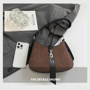 Detail of suede crescent bag with gold metal buckle resting on a gray suit jacket