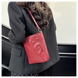Vue détaillée du sac seau rouge foncé avec texture gaufrée sur fond de blazer noir