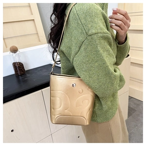 Détail d'un sac seau doré métallisé avec lettre en relief, porté sur un pull vert