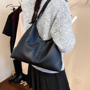 Grand sac à main minimaliste en cuir noir porté par un mannequin dans un cadre intérieur