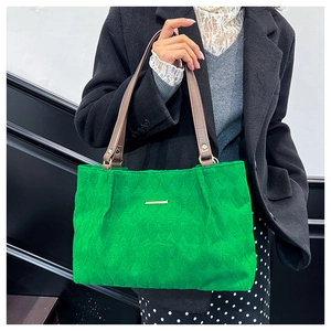 Detail of green wavy-quilted tote bag with gold accent and brown leather handles