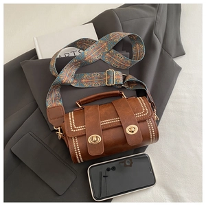 Close-up of vintage brown cylinder crossbody bag with golden studs and ethnic strap