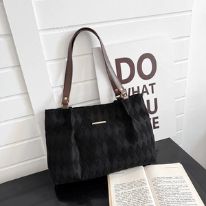 Detail of black quilted tote bag with brown straps against a minimalist backdrop