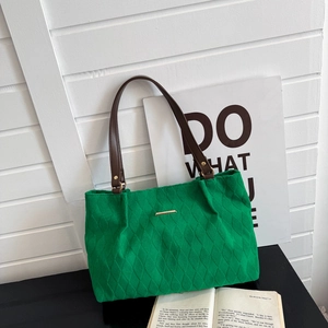 Detail of green quilted tote bag with brown leather handles and gold metal logo plate