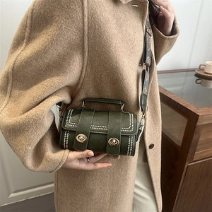 Dark green crossbody bag with silver studs and patterned wide strap on camel coat
