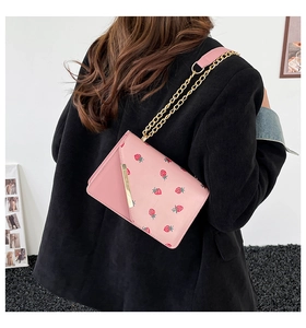 Pink crossbody bag with strawberry print and gold chain strap shown on black corduroy jacket