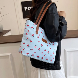 Light blue tote bag with red cherry prints and brown leather handles on shoulder
