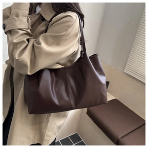 Detail of soft coffee leather tote bag with vertical stitching on a model in trench coat