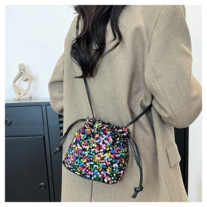 Dettaglio di una borsa a secchiello con paillettes colorate su un blazer beige