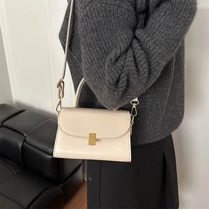 Minimalist beige crossbody leather square bag with gold buckle on shoulder of model