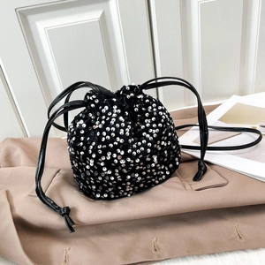 Dettaglio di una borsa a secchiello nera con coulisse e paillettes argento su un trench