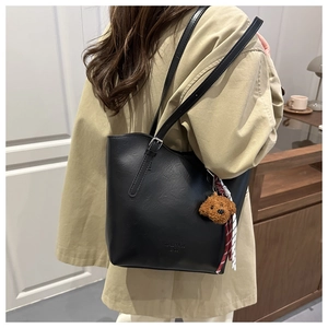Detail of black leather tote bag featuring a cute bear charm and adjustable shoulder strap