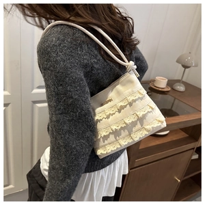 Detailed view of cream lace shoulder bag worn by model in a cozy indoor setting