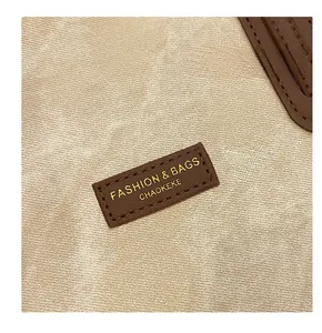 Close-up of the premium leather logo tag on a textured khaki and brown tote bag