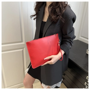 Detailed view of a bright red faux leather clutch bag with a zipper and hand strap
