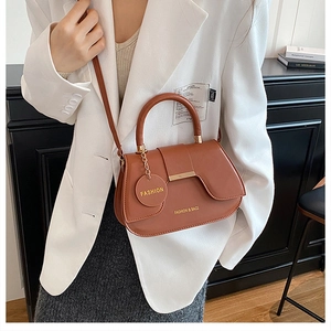 Caramel leather saddle bag with top handle and gold lettering shown on a model